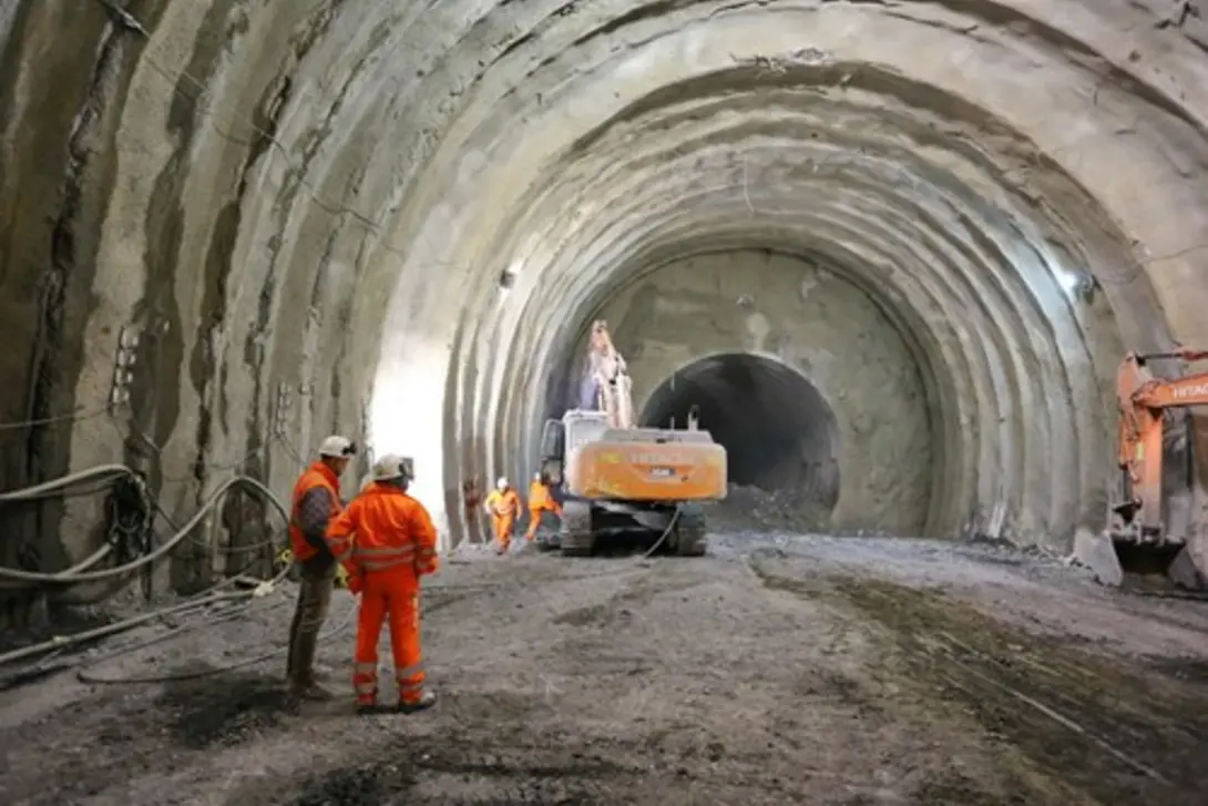 Workers applying SprayMasta shotcrete inside a large underground tunnel using excavators and spray equipment for structural support and lining stabilization.