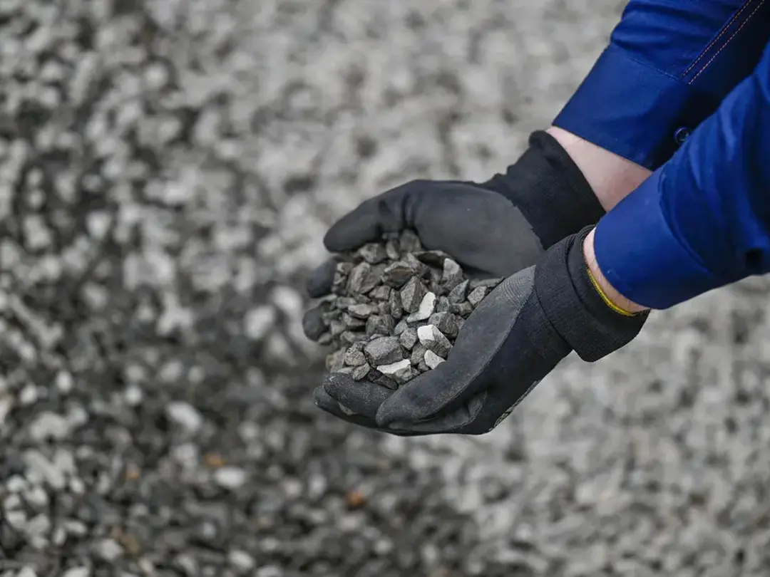 Gloved hands holding recycled aggregate material at a quarry site.